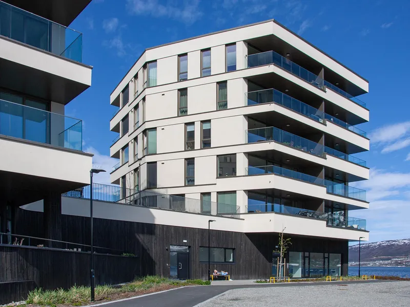 Fasaden på Alfon C med store balkonger og lysinnslipp, plassert tett ved sjøen på Kræmer Brygge.
