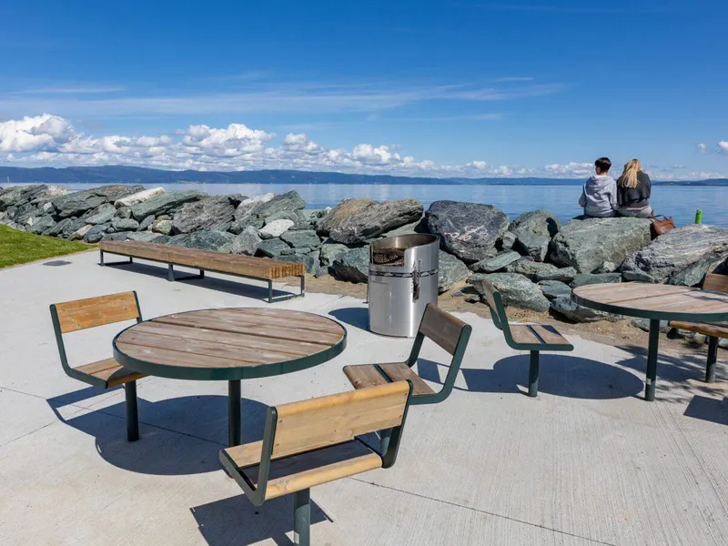 En oppholdssone med betongdekke, med benker, bord og en utegrill i blank stål. Foto: Asplan Viak