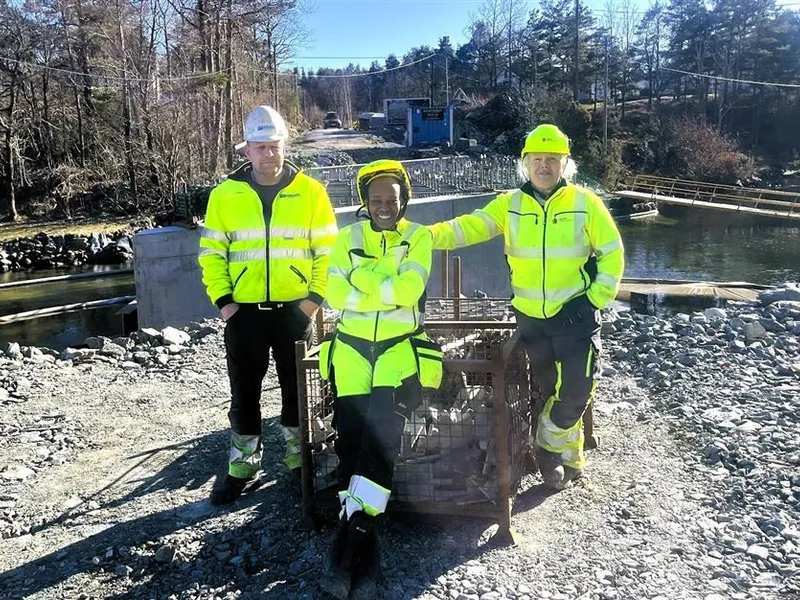 Tre arbeidere sitter og står på den ene enden av en bru som er under oppføring - Klikk for stort bilde