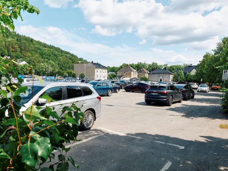 Parkeringsplass med flere biler og store murhus i bakgrunnen. Foto