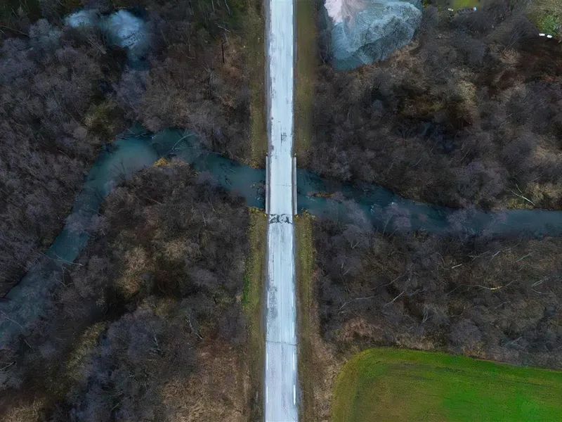 Et dronefoto av en eldre bru langs en fylkesveg. Bildet er tatt om høsten. - Klikk for stort bilde