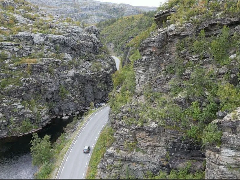 Bildet er et dronebilde av E45 der vegen slynger seg langs Eibyelva igjennom  en canyon med stupbratte fjell på begge sider. Bildeteksten sier, Flaskehalsen: Dagens E45 gjennom kløfta følger en naturlig elvecanyon. Den skjærer seg dypt ned i fjellet fra Finnmarksvidda mot Alta. Fjellet har dårlig kvalitet og det går ofte snøskred, sørpeskred og steinras som gir stengt veg. Nå skal strekningen legges i tunnel.