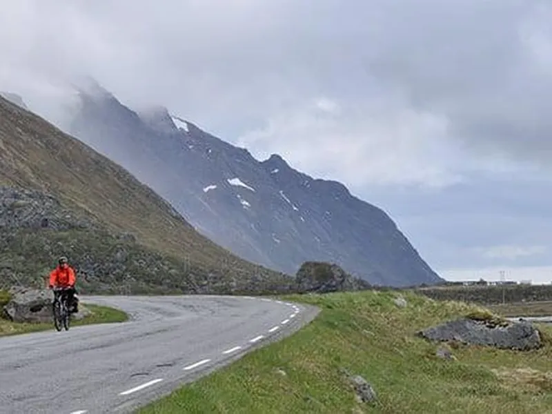 Syklist på veg med fjell og fjord i bakgrunnen.