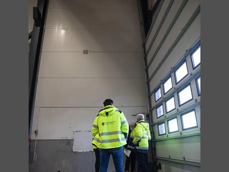 Et par menn i vernejakker står i en større hall. - Klikk for stort bilde