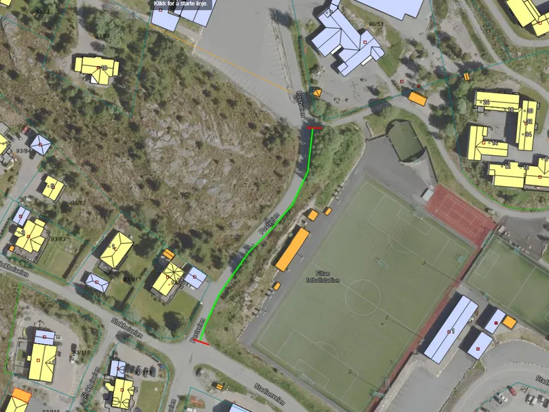 Aerial view of a neighborhood with buildings, roads, and a sports field. Paths and structures are marked in various colors.