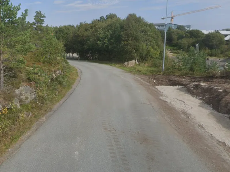 A winding road surrounded by greenery, with construction visible on the right side and a clear blue sky above.