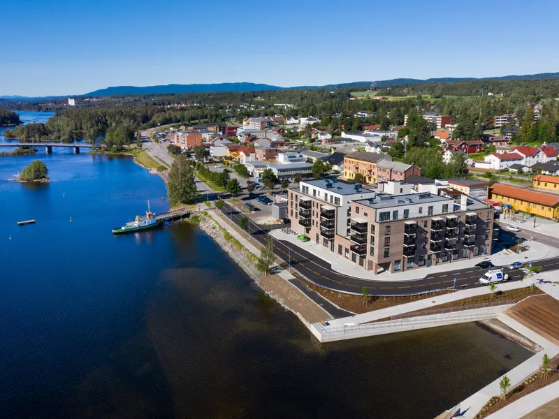 Dronefoto med vannet i forgrunn, prosjektet og togstasjonen like bak prosjektet