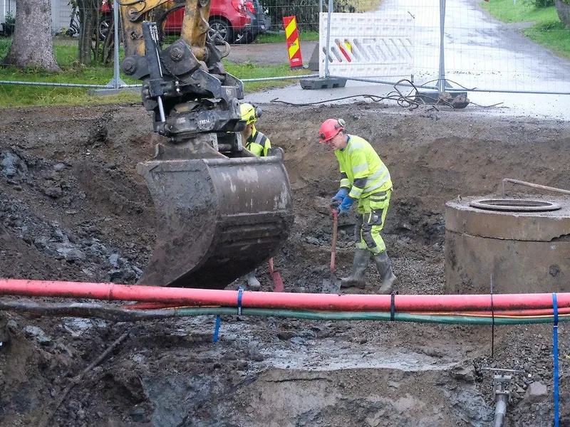 Man og gravemaksin graver i bakken med ledninger rundt.