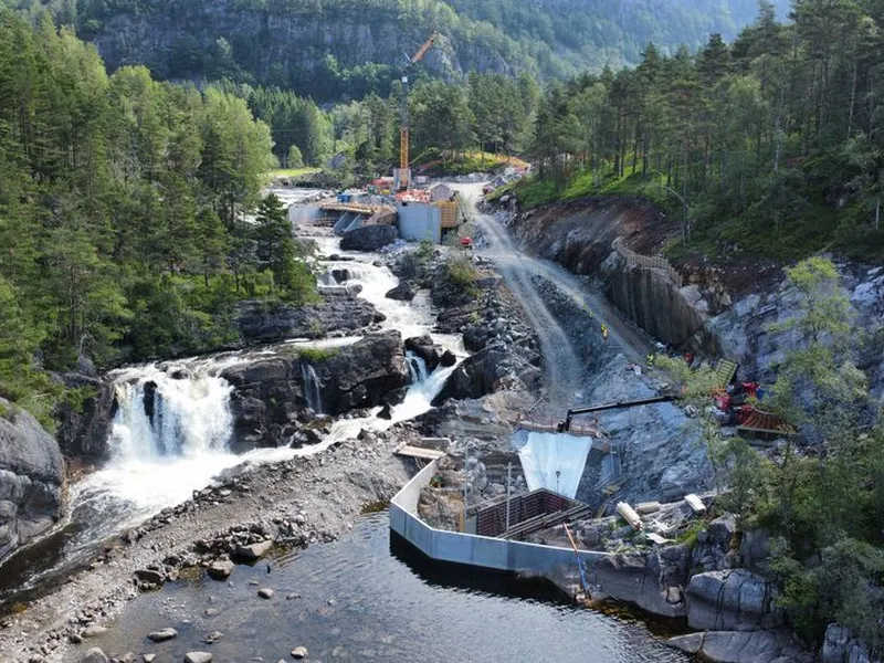 Anleggsområde, anleggsmaskiner, foss, vann, skog. Foto.