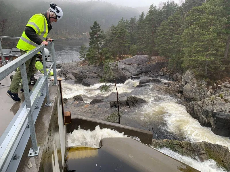 Foss, dam, vann, to mennesker i arbeidsklær, fuglekasse. Foto.
