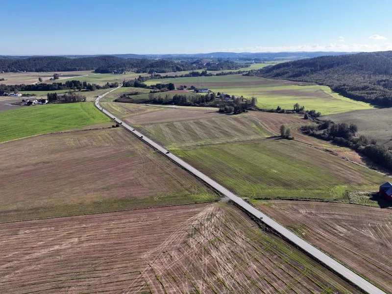 Stort dronebilde som viser Bispeveien fv.35 omgitt av jorder. Bildet er tatt fra Vivestad mot Ås.