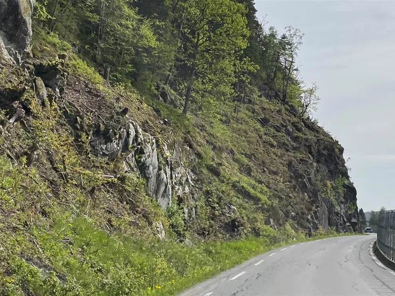 Foto av parti av fv. 3718 Bøylestadveien med høy fjellskjæring og jernbane tett inntil vegen - Klikk for stort bilde