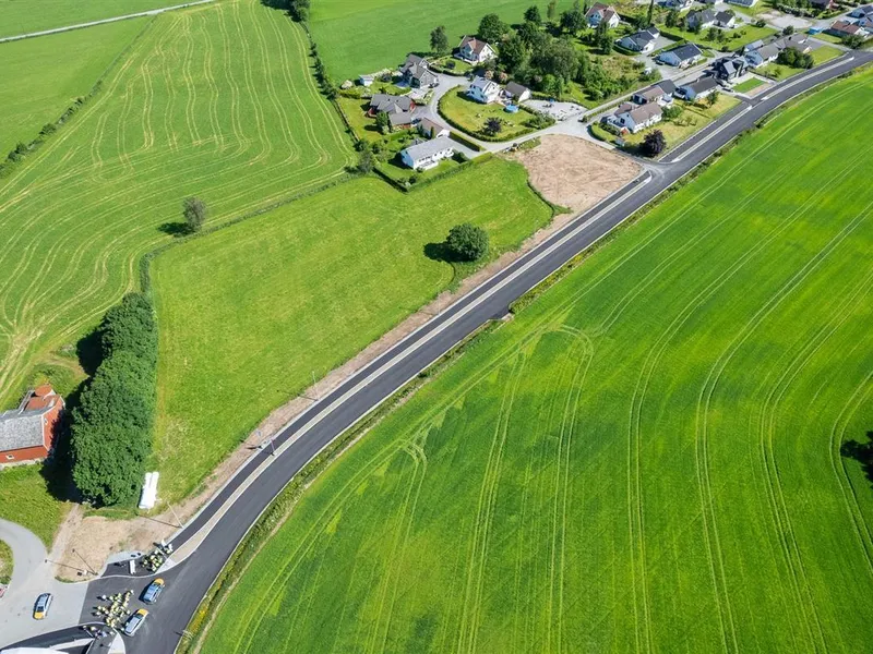 Droneutsnitt av vei med grønne jorder rundt. Foto - Klikk for stort bilde
