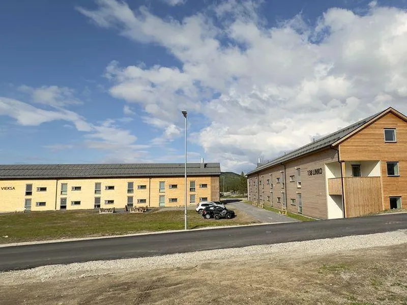 To bygninger med moderne design ved en vei under en blå himmel.