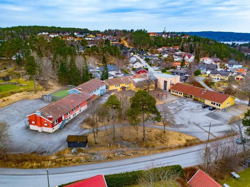Dronebilde av skolebygg i rødt og gult med skolegård rundt.  - Klikk for stort bilde