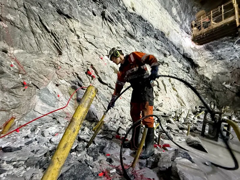 Bildet viser lærling Trond Randen i arbeid med å lade en salve inne på stuff (fjellveggen som skal sprenges ut og bli tunnel). Bildetaksten sier, Skanska passerer 15 000 meter drevet tunnel på OPS Hålogalandsvegen.  I marmorhvelvet i Gullberg øst, som vender ut mot Tjeldsundbroen står lærling Trond Randen (fra Sel i Gudbrandsdalen) og lader klart for dagens første salve.