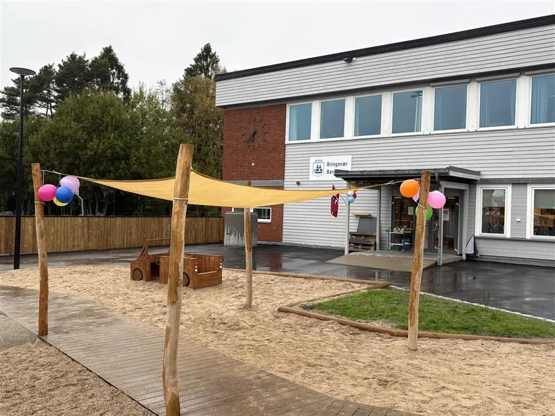 Et stort seil over et gruslagt område ved et barnehagebygg. - Klikk for stort bilde