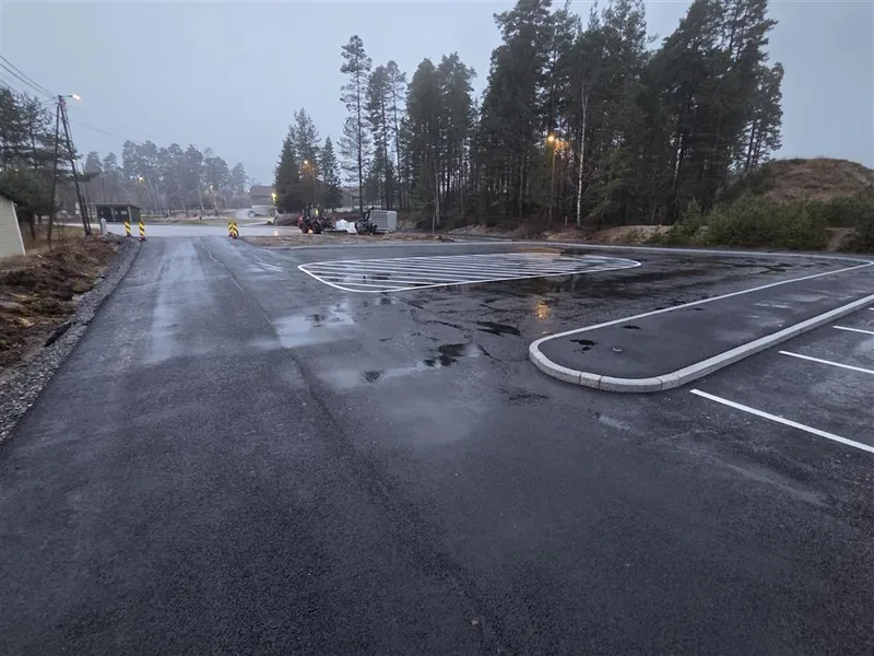 Bilde som viser den nyasfalterte parkeringsplassen mellom Otrahallen og Hornnes barneskule. Her har det blitt oppgradert iht trafikksikkerhetshensyn. Det har kommet ny drop-off-sone, parkeringsplass, gangveg for myke trafikanter og leveringssone for buss. - Klikk for stort bilde
