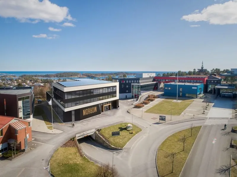 Oversiktsbilde av Morrow Battery Innovation Centre (BIC) på Campus Grimstad, med moderne bygg, campusområde og sjøen i bakgrunnen.