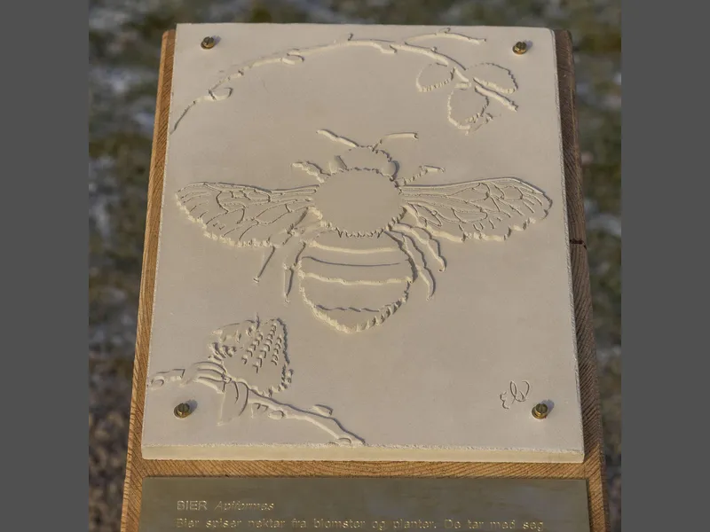 betongplate med avtrykk av en bie. Platen er montert på en trestokk.