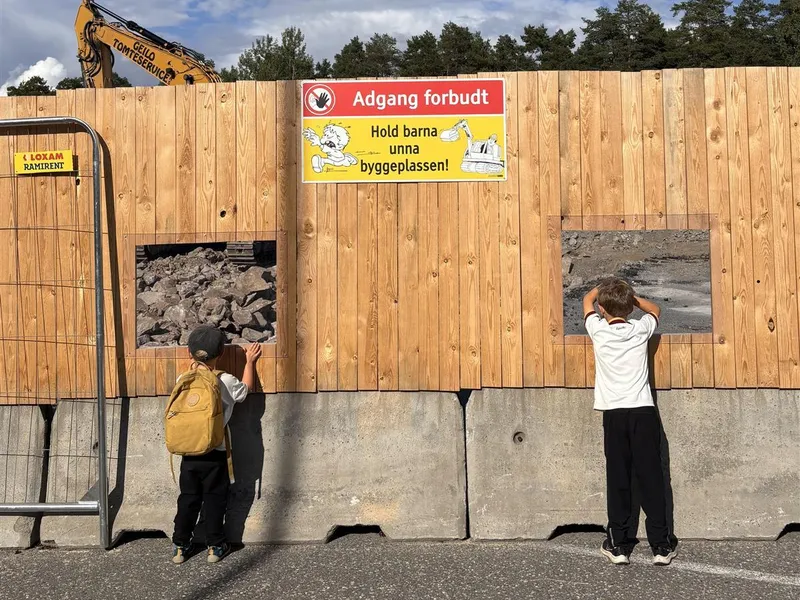 Byggeplassen er inngjerdet, to barn kikker på skiltene - Klikk for stort bilde