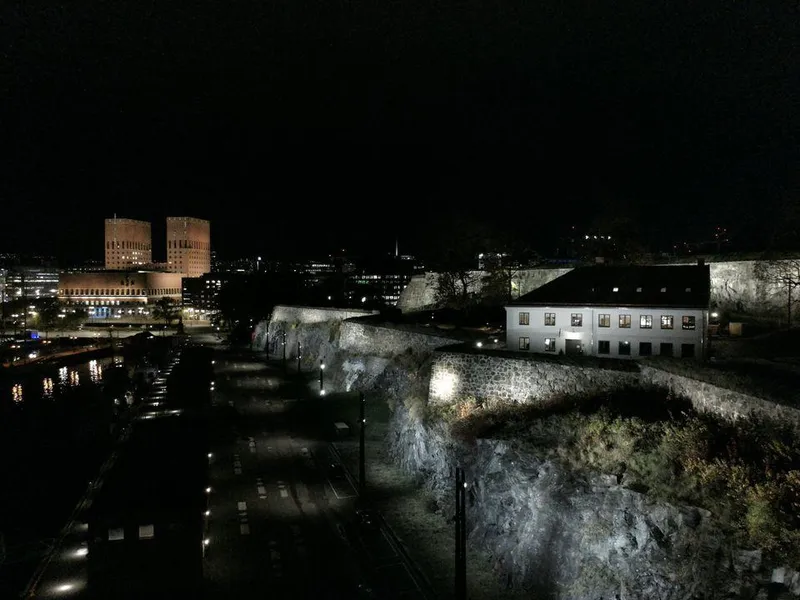 Bilde av Akershus festning i forgrunnen, med Oslo rådhus i bakgrunnen, nattbelysning.