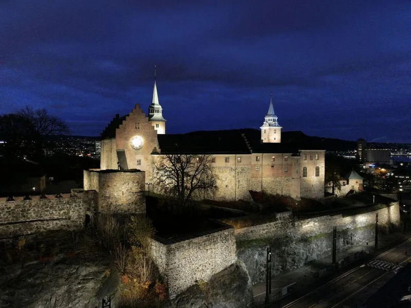 Akershus festning opplyst om natten, med to tårn synlige mot en mørk himmel.