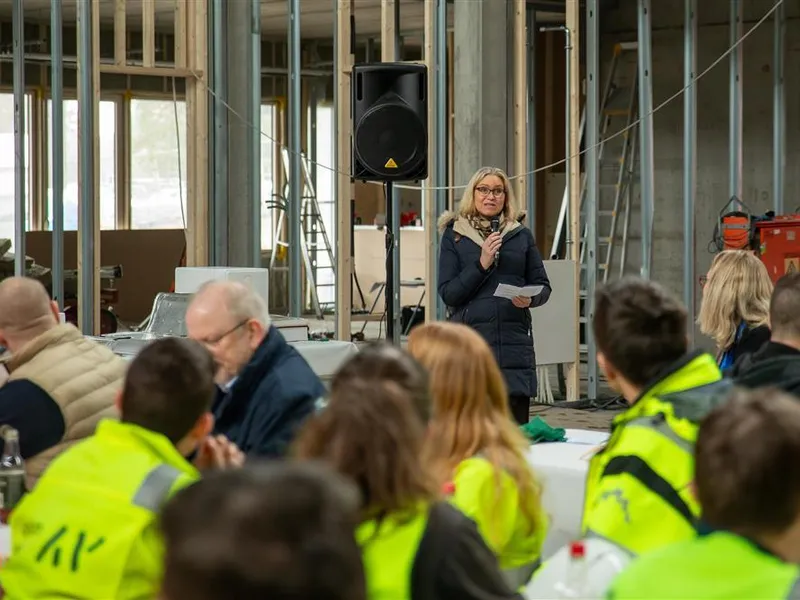 Beate Skretting prater i mikrofon til arbeiderne inne på det soms kal bli nye Fjære barneskole.  - Klikk for stort bilde