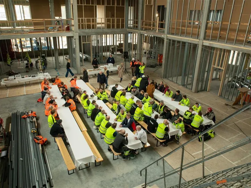 Oversiktsbilde fra 2. etasje på det som skal bli nye Fjære barneskole. Nede på betonggulvet ser vi fire langbord og mange mennesker.  - Klikk for stort bilde