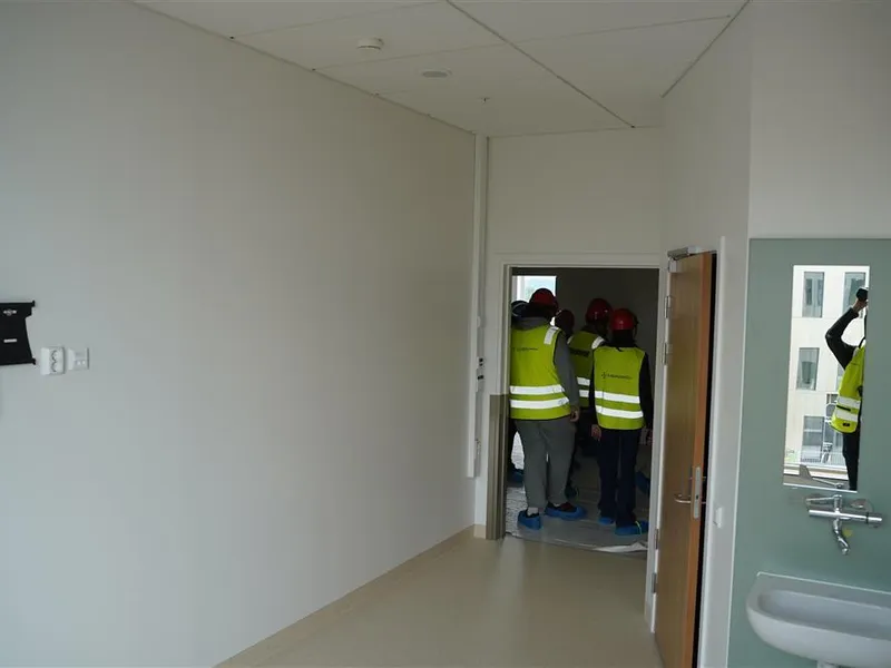 Umøblert pasientrom i hvit med inngang til bad, vask og speil på veggen - Klikk for stort bilde