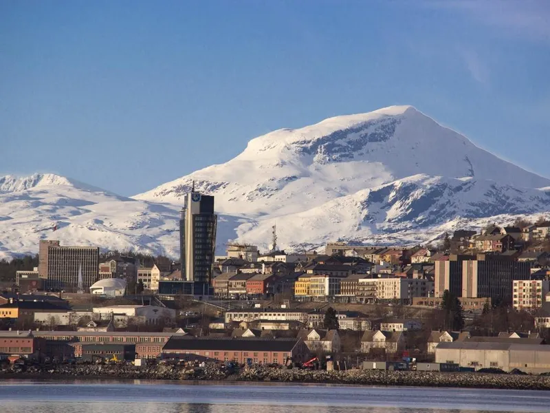 Skyline med by, snøkledte fjell i bakgrunnen. - Klikk for stort bilde