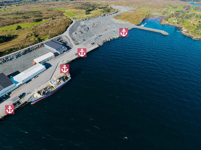 Blå sjø, stor kai med bygninger og lynglandskap rundt - Klikk for stort bilde