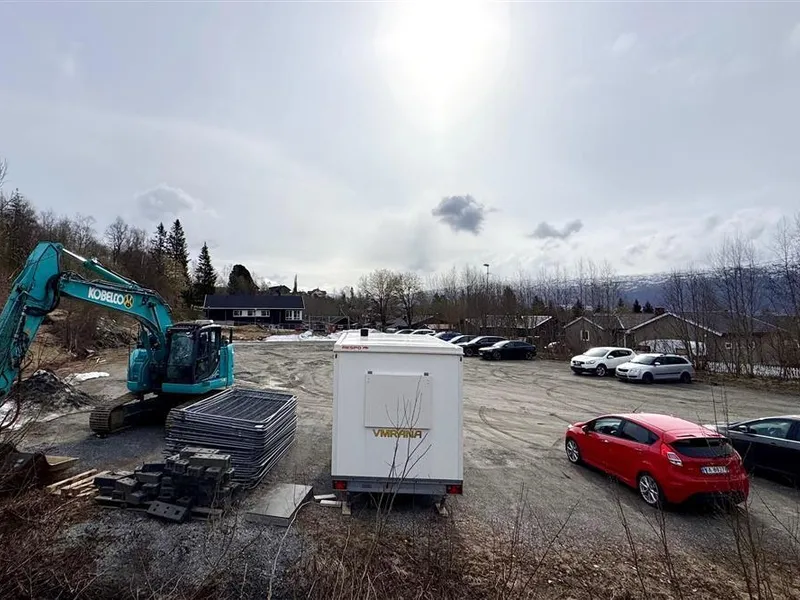 Parkeringsområde med biler og gravemaskin.  - Klikk for stort bilde