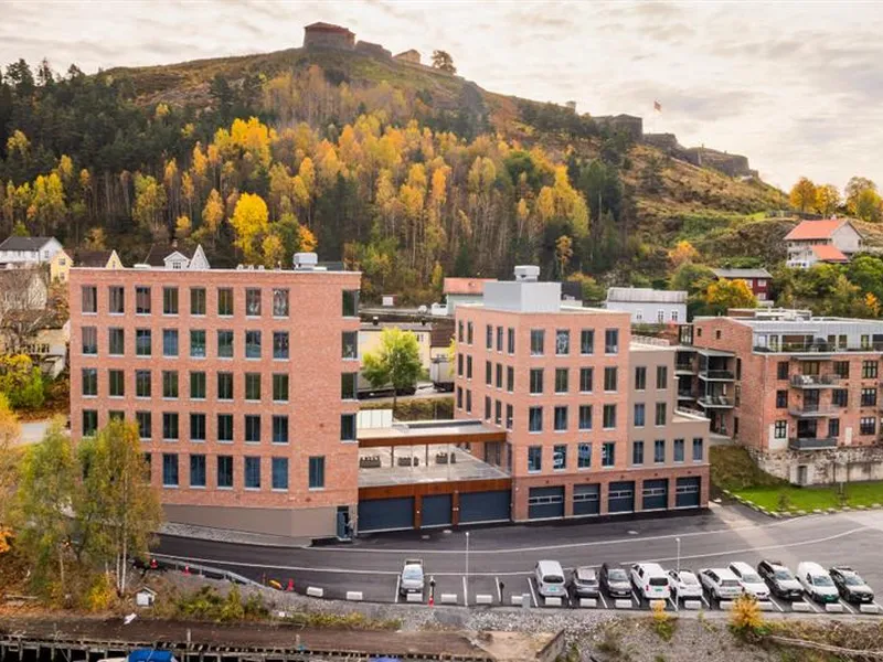 Utendørs bilde av murbygninger i forkant og Fredriksten festning i horisonten bak. - Klikk for stort bilde
