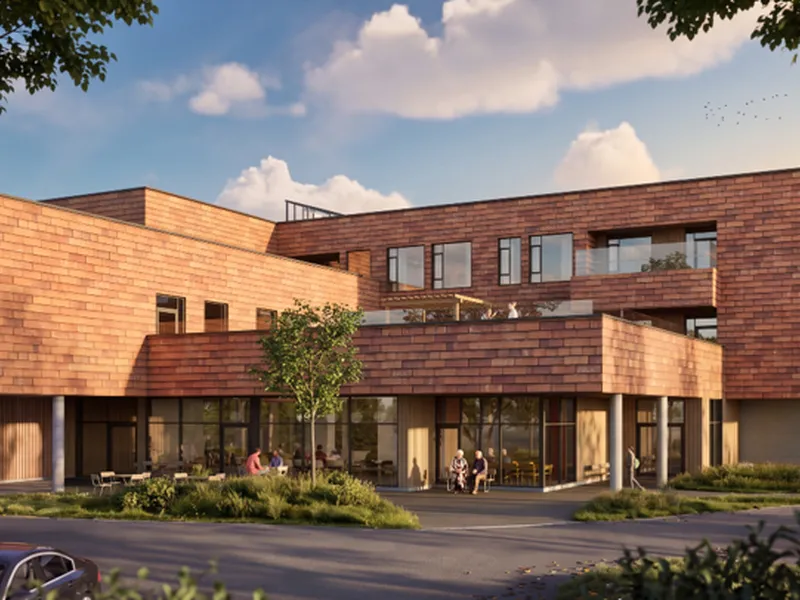 Nytt sykehjem på Bergenhus 2026. Et moderne mursteinshus med balkonger og uteplass. Flere personer sitter på møbler utenfor.