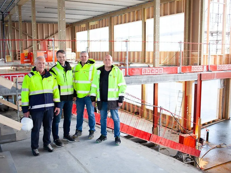 Bildet viser fire personer som står skulder ved skulder i et råbygg.