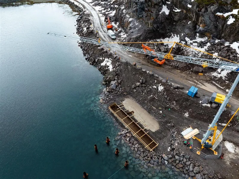 En anleggssone ved en fjord, fotografert fra lufta med drone.  Man kan se en kran ruve over anleggsplassen. - Klikk for stort bilde