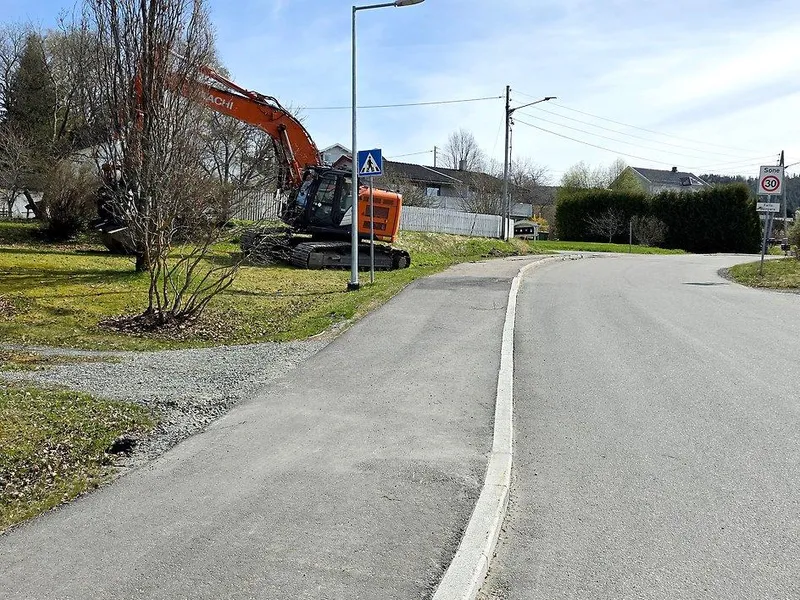 Bildet viser en vei og et gangfelt. Ved siden av står en gravemaskin.