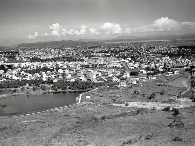 Flyfoto i svart hvitt over et tjern med park rundt og bebyggelse rundt parkområdet.