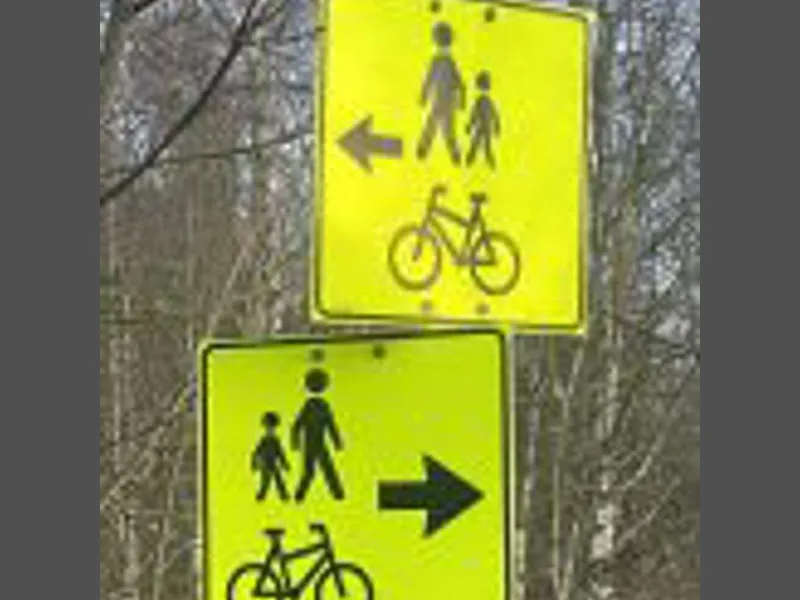 To gule skilt med svarte piler som viser omvei for syklister og fotgjengere.