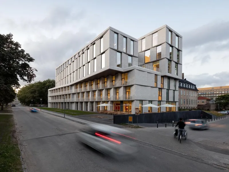 Bygning i lys stein i gatemiljø med bilist og syklist. Foto