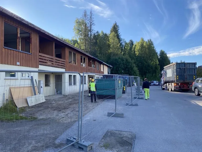 Bygningsarbeidere og kjøretøy er foran et rekkehus med en brannskadet del - Klikk for stort bilde
