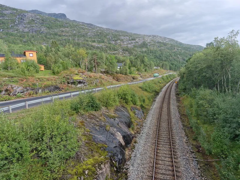 Bildet viser at rv. 80 og Nordlandsbanen går parallelt mange steder. Bildeteksten sier, Krevende utbygging: Næhet til Nordlandsbanen og liten plass mellom skinnegang, veg og bebyggelse gjør utbyggingen mer krevende.