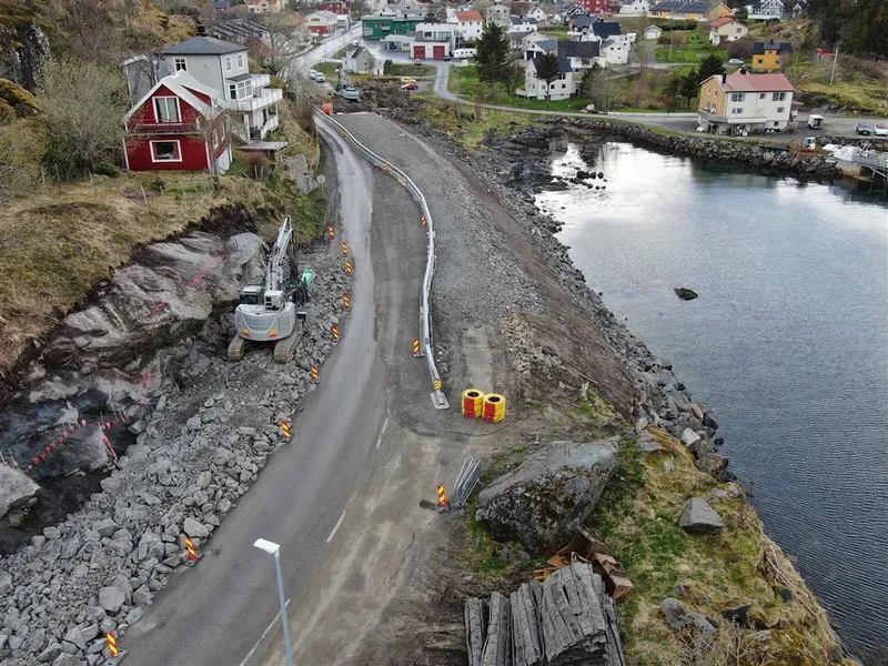 Smal veg mellom berg og fjord.Anleggsaktivitet. Hus i bakgrunnen. Foto - Klikk for stort bilde
