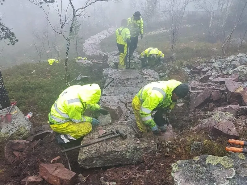 Fem menn i gule arbeidsklær bygger steintrapp i regn og tåke - Klikk for stort bilde