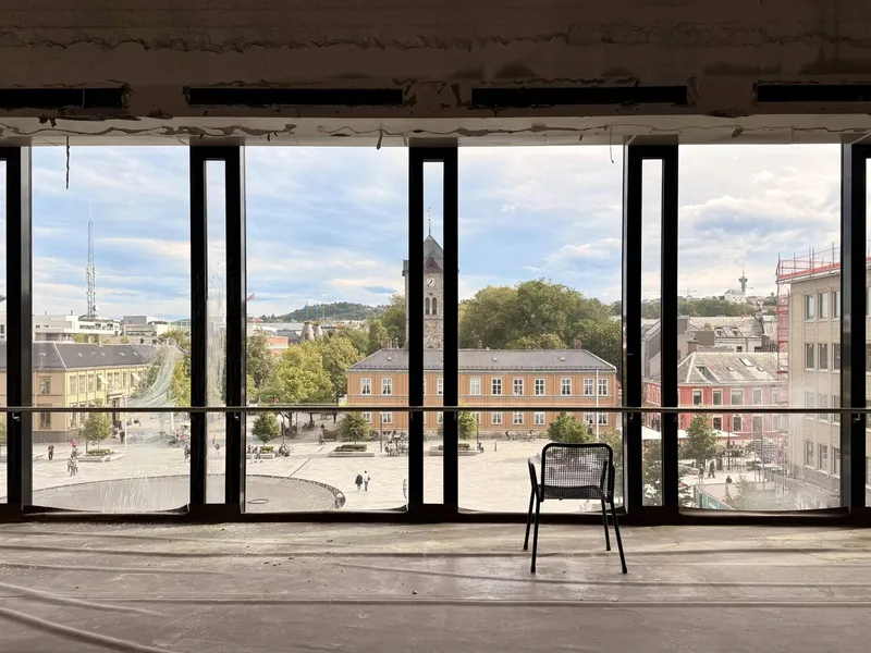 Utsikt fra et lokale under rehabilitering ved Trondheim Torg, der Asplan Viak bidrar i prosjektet, med store vindusflater mot torget og Trondheim sentrum.