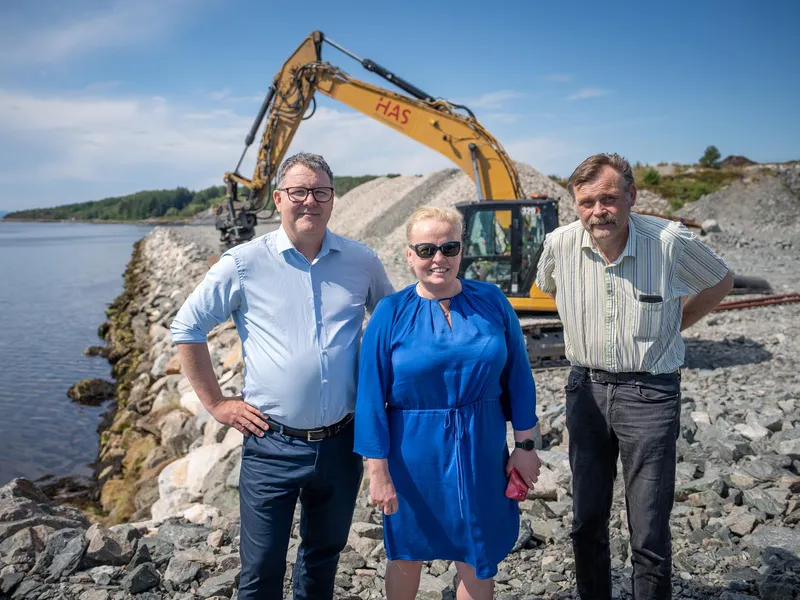 Mennesker foran gravemaskin smiler til kamera.