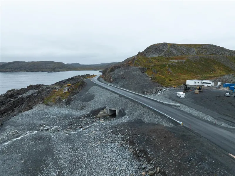 Et dronefoto av en ny bru over en mindre elv. Man kan se ny kulvert, rekkverk og asfalt. Bildet er tatt på høsten. Det er overskyet. - Klikk for stort bilde